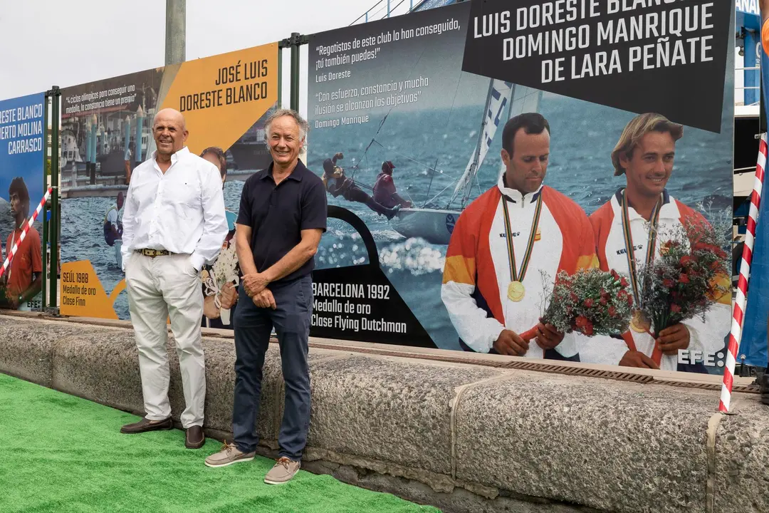 Los regatistas Luis Doreste (d) y Domingo Manrique (i), medallas de oro de vela en los Juegos de Barcelona de 1992 en la clase flying dutchman, posan ante una foto suya de EFE en el mural que el Real Club N&aacute;utico de Gran Canaria ha instalado en la rampa donde embarcan sus tripulaciones para inspirar sus su j&oacute;venes promesas con los logros de sus ol&iacute;mpicos. EFE/Quique Curbelo